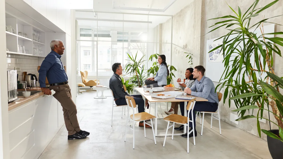 Employees eating together and talking in an office workplace cafeteria.