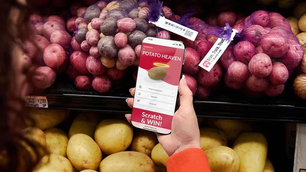 Women with smartphone in hand with text "Potato Heaven" written on screen, infront of a aisle with potatoes