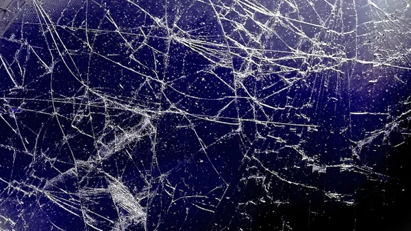 In a close-up of a severely shattered monitor screen, the display contains blue and black hues with various-sized white cracks. 