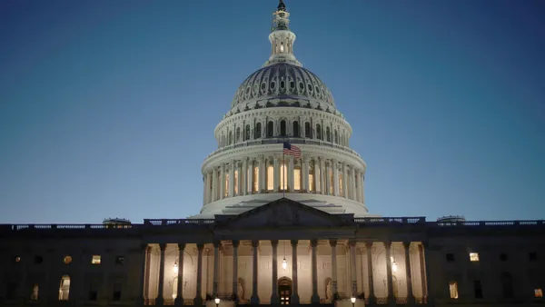 A domed classical building is lit up in the evening against a dark blue sky, with an American flag waving out front.