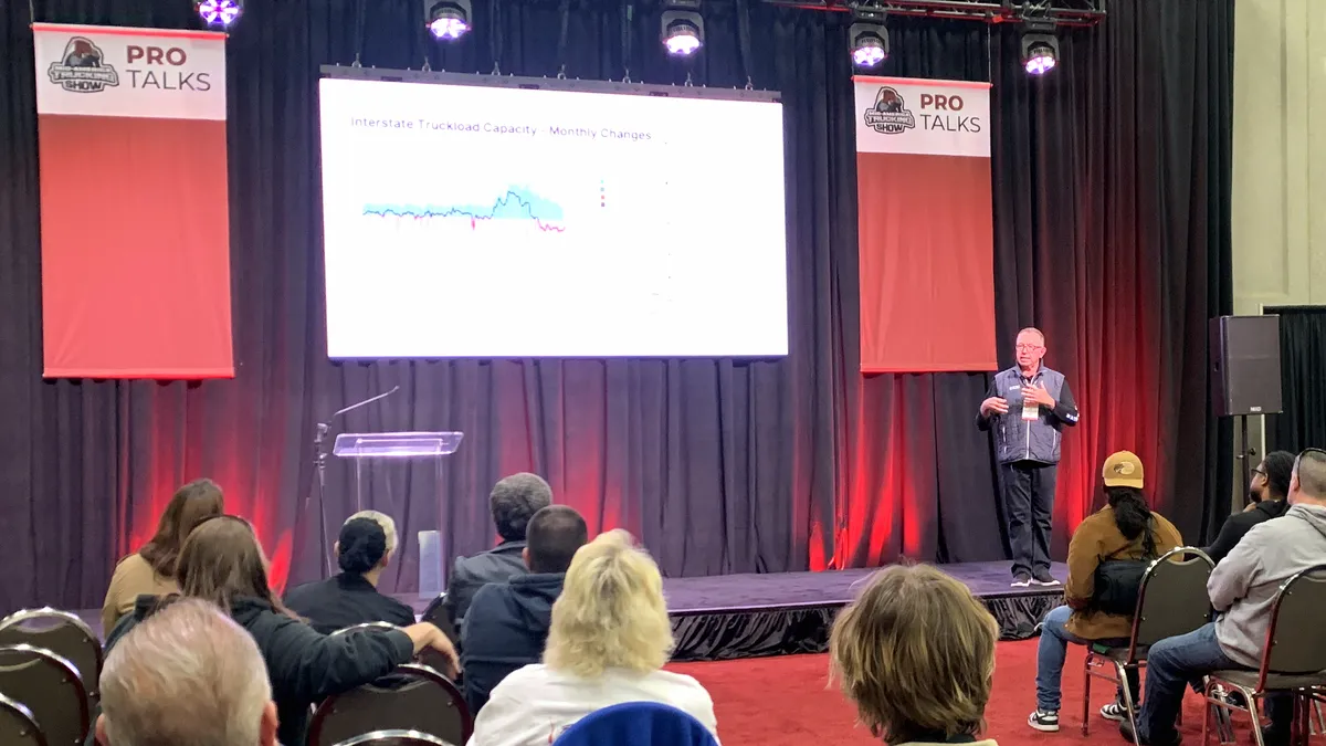 DAT Principal Analyst Dean Croke talks to audience members at a stage in the Kentucky Exposition Center.