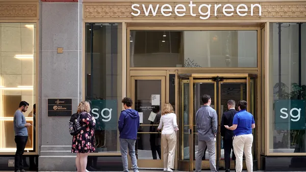 People wait in line to enter a building with a sweetgreen logo at the top.