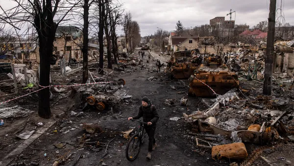 A man pushes his bike through debris and destroyed Russian military vehicles on a street on April 06, 2022 in Bucha, Ukraine.