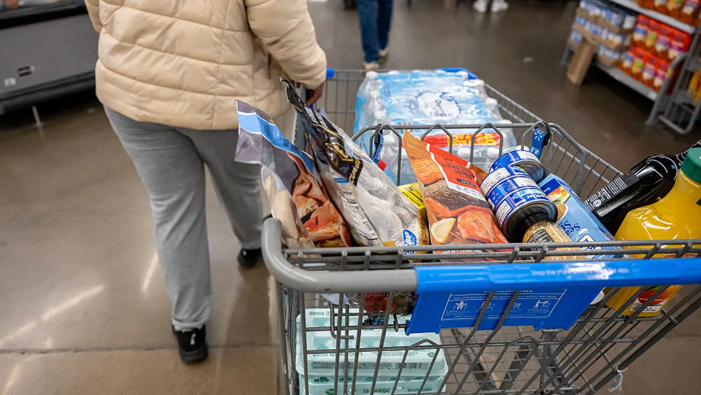 A person walks alongside a shopping cart filled with groceries.