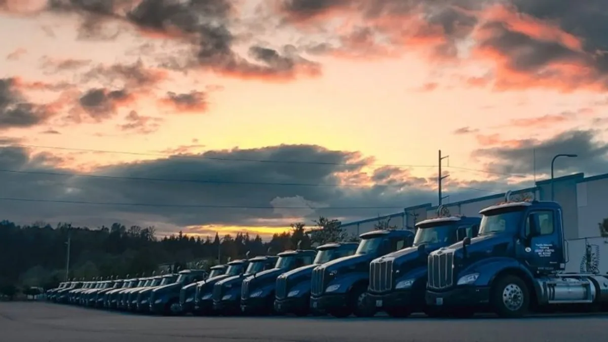 A line of Pacific Cascade trucks are parked outside a facility.