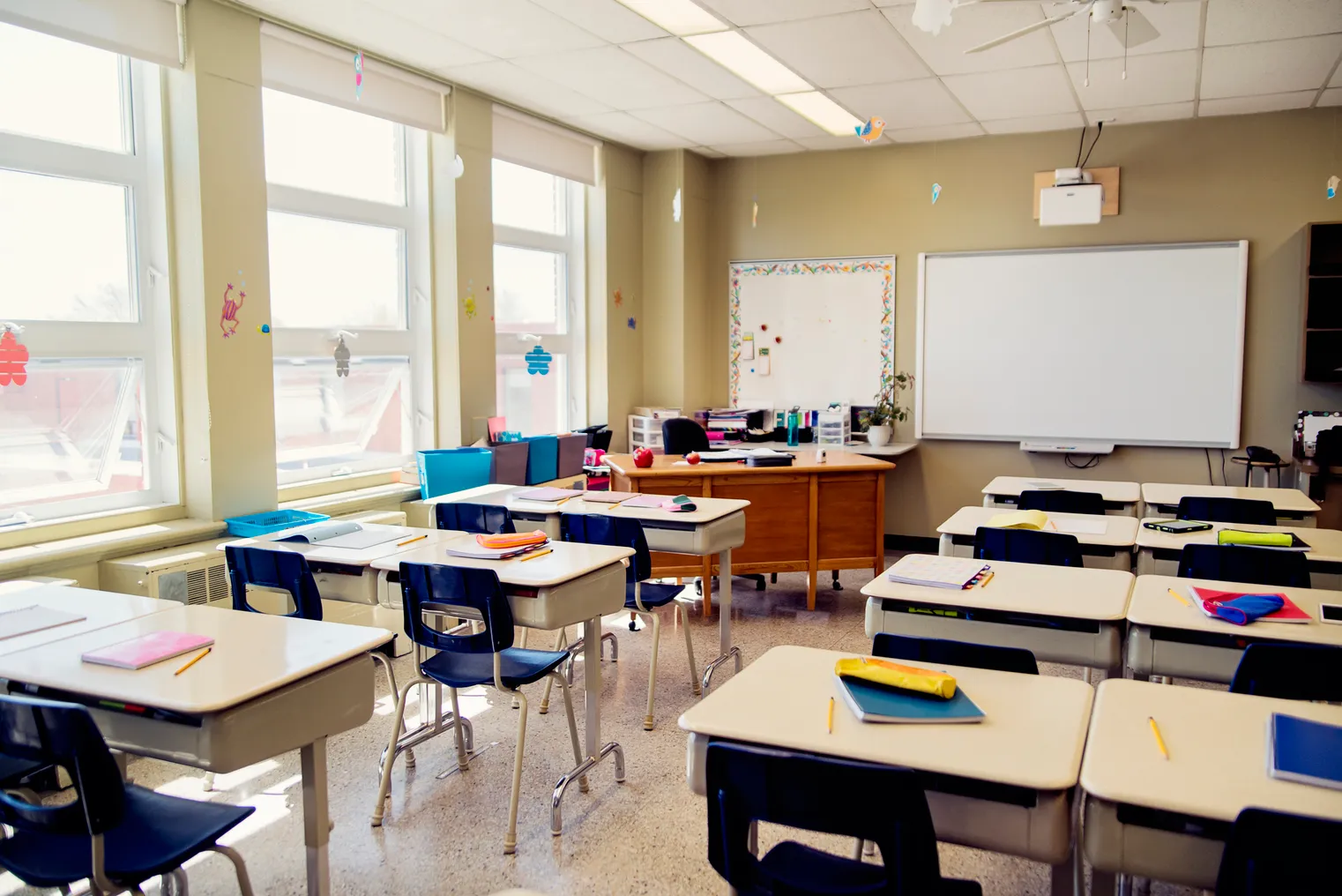 An empty elementary classroom which includes an interactive whiteboard at the side of teacher’s desk.