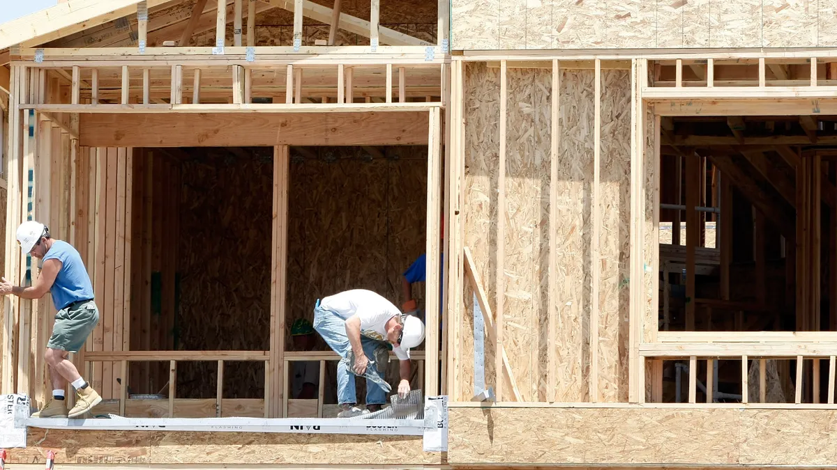 The photo shows two construction workers wearing hard hats building a house.