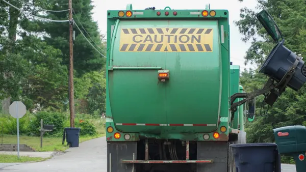 Rear view of a waste truck, with the word caution on its body, collecting a cart in a residential area