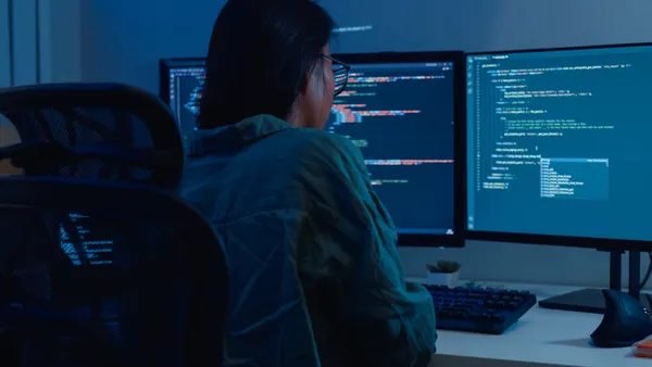software developers using computer to write code sitting at desk with multiple screens work remotely in home at night.