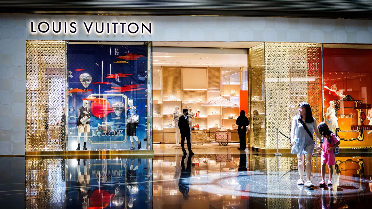 A well-lit store in an indoor mall has a sign in the front reading "Louis Vuitton."