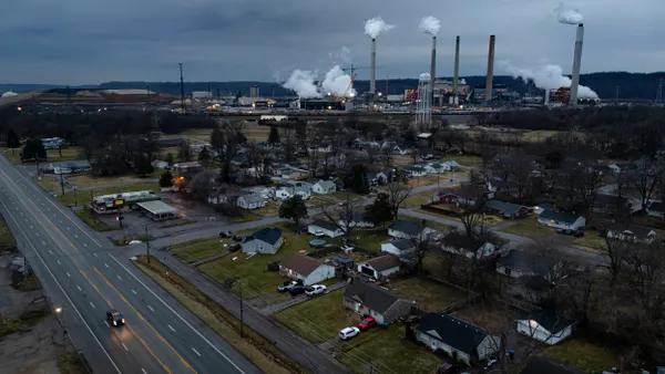 A power plant emitting smoke from smokestacks surrounded by a neighborhood with a street in the foreground.