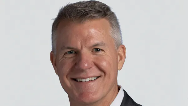 A person smiles at a camera in front of a gray background.