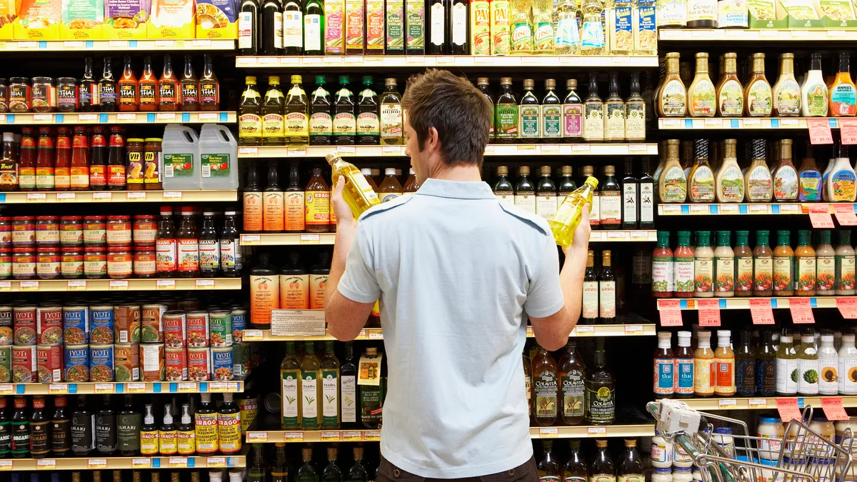 Young man in supermarket comparing bottles of oil.