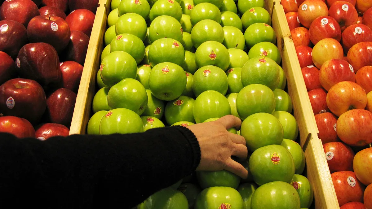 Apples at a grocer store with a hand reaching for one