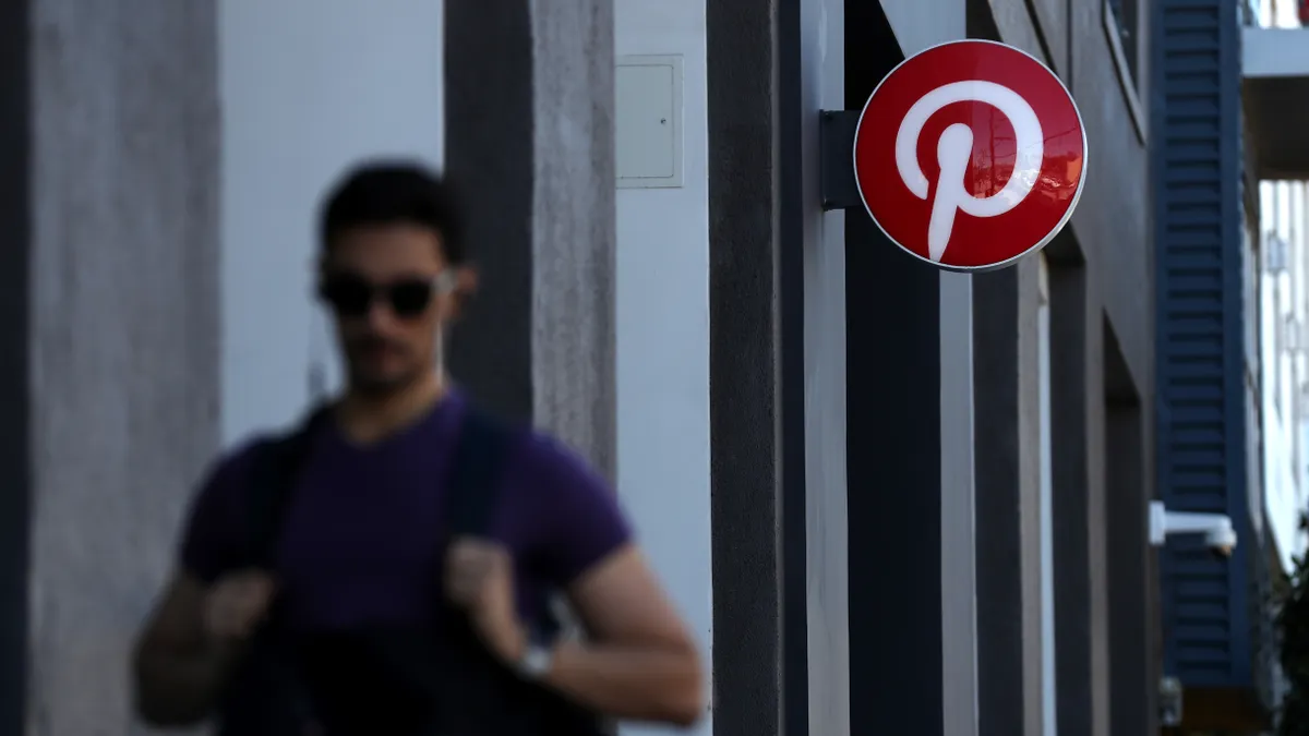 Person with sunglasses walking down street in front of a building with a red and white logo