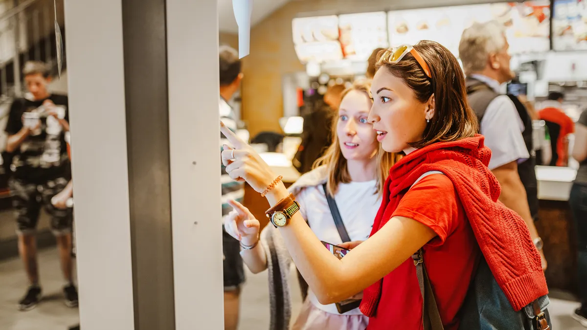 A woman orders food in the touch screen terminal with electronic menu in fast food restaurant