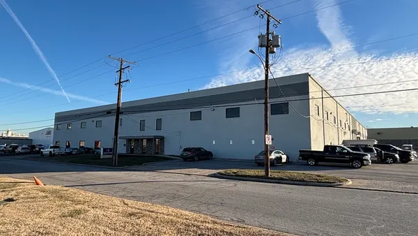 A bare building is somewhat obscured by power lines behind a road on a clear, sunny day.