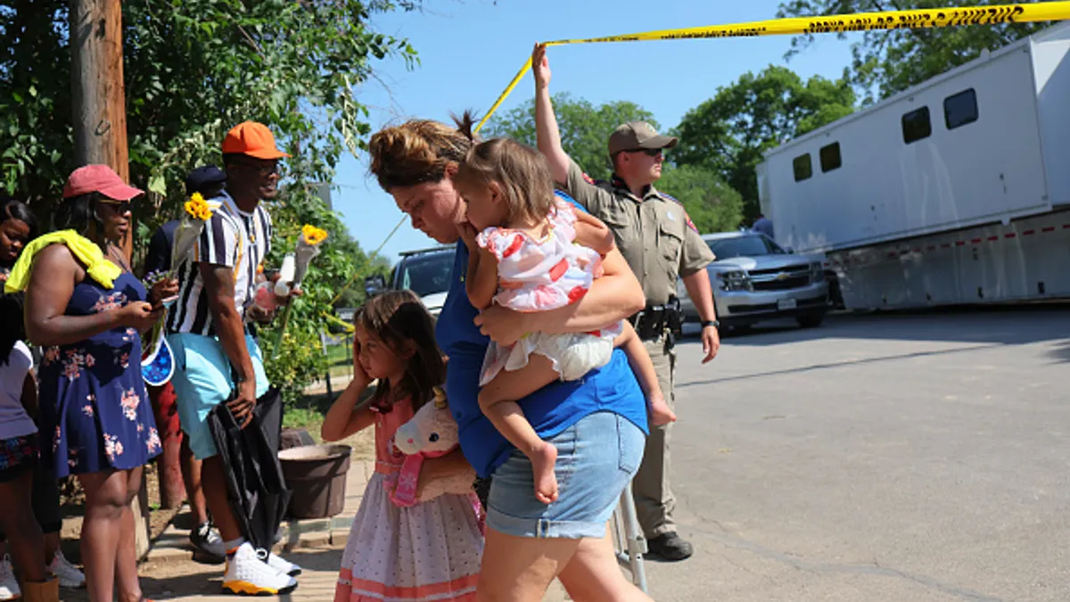 A Department of Public Safety State Trooper lifts a police tape as woman and young children cross under it at a memorial to the victims of the Robb Elementary School mass shooting on May 28, 2022 in U