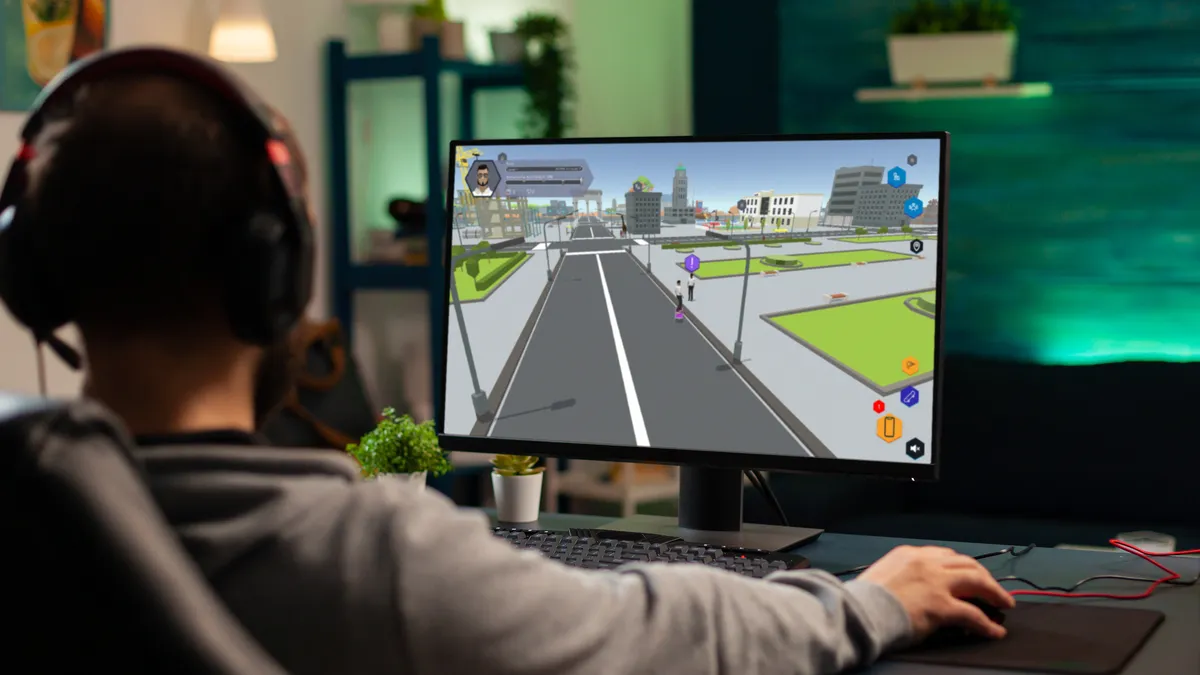 A person with headphones on looks intently at computer screen with simulated road on it.