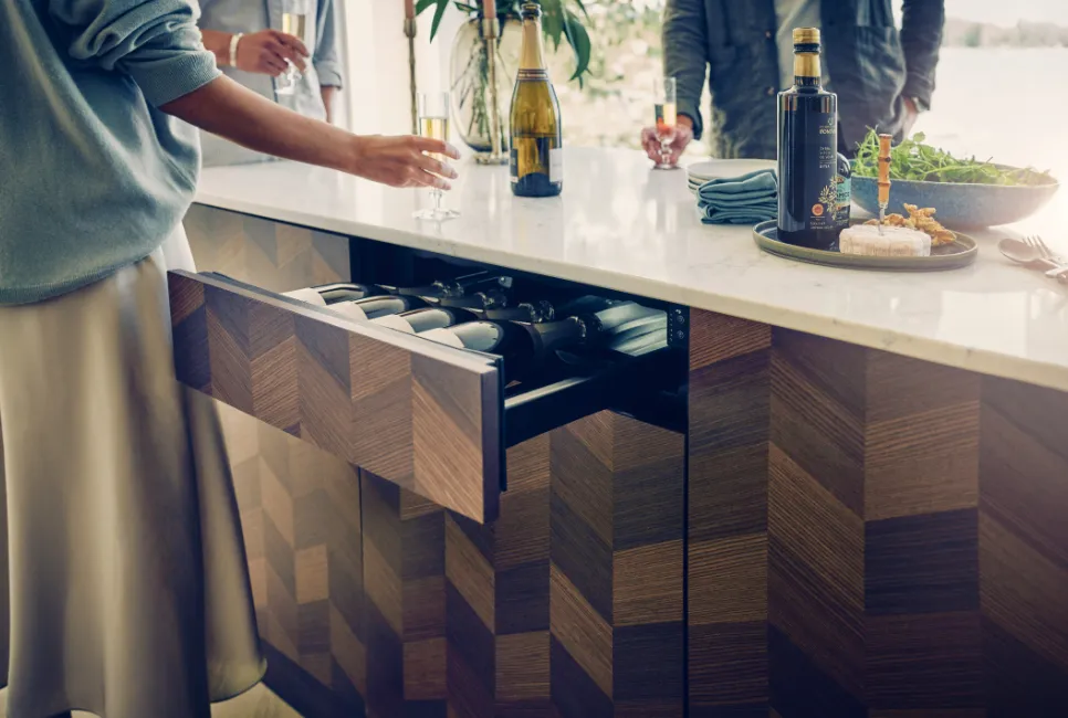 A kitchen drawer is open to reveal five wine bottles inside.