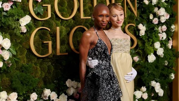 Two people stand next to each other holding each other's waists, dressed in evening clothes and standing in front of a sign that reads Golden Globes.