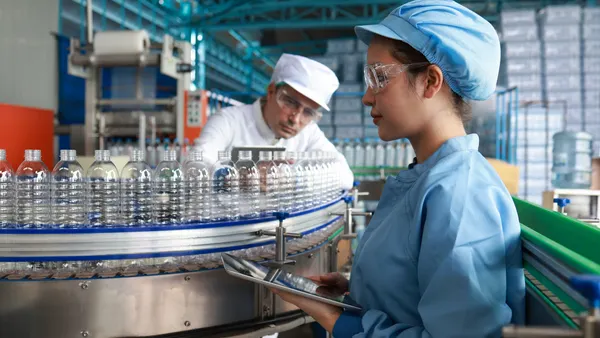The lab technicians and hygienists with clean suits and PPE examining water bottles in bottling plant mineral water drinking water factory