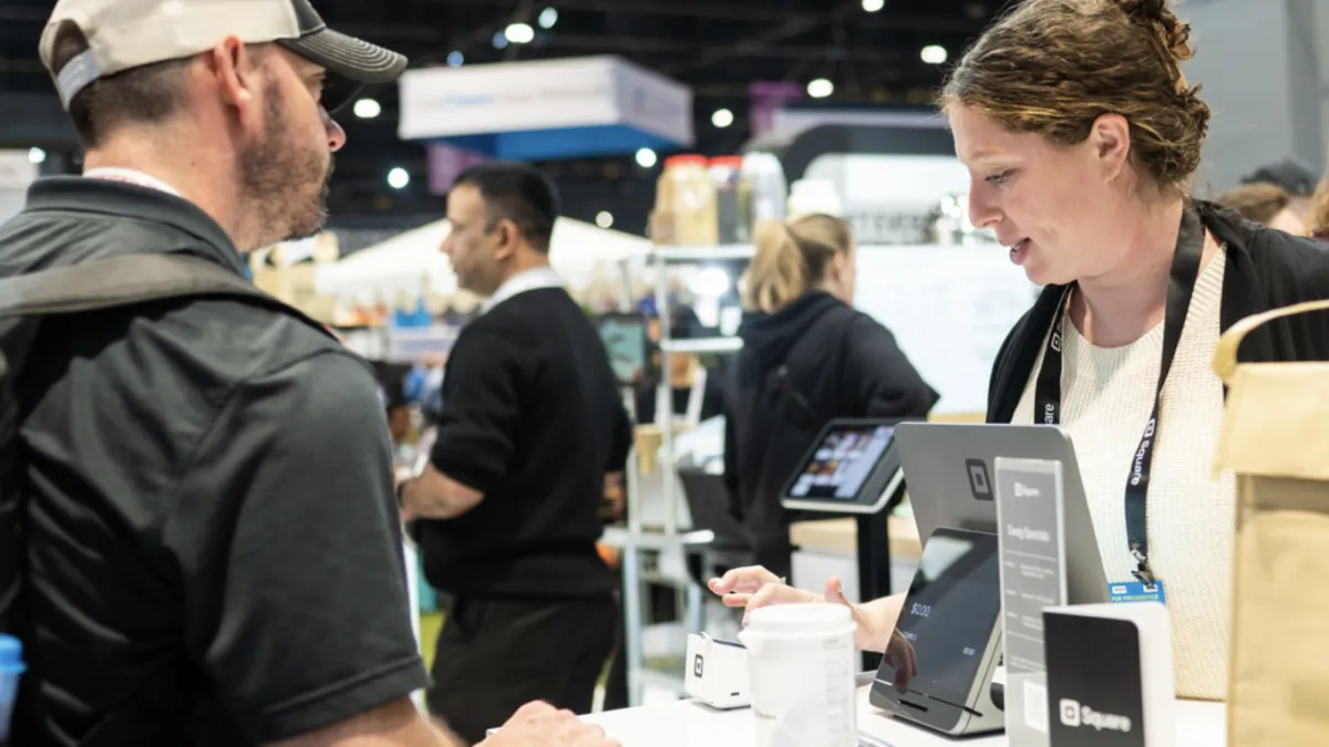 Two people at an event, one of them is using a Square kiosk to pay for something.