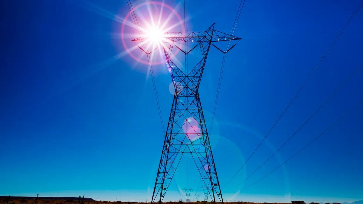 High voltage electricity transmission tower back lit by sun with lens flare.