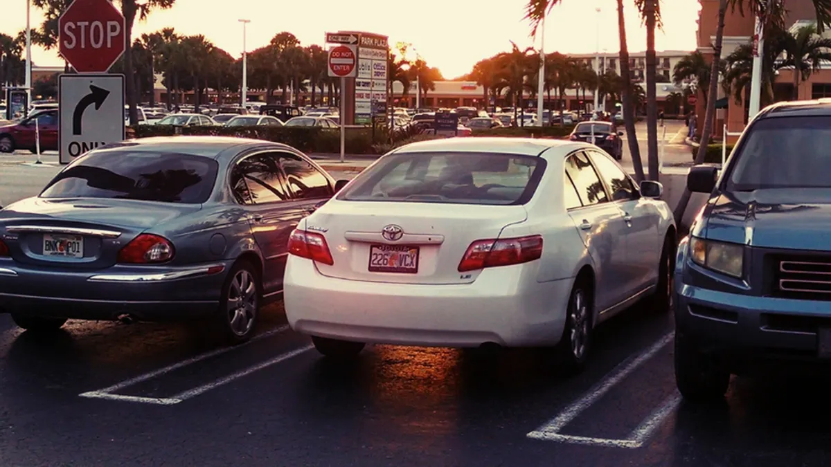 A row of cars parked in a parking lot outside of a shopping center.