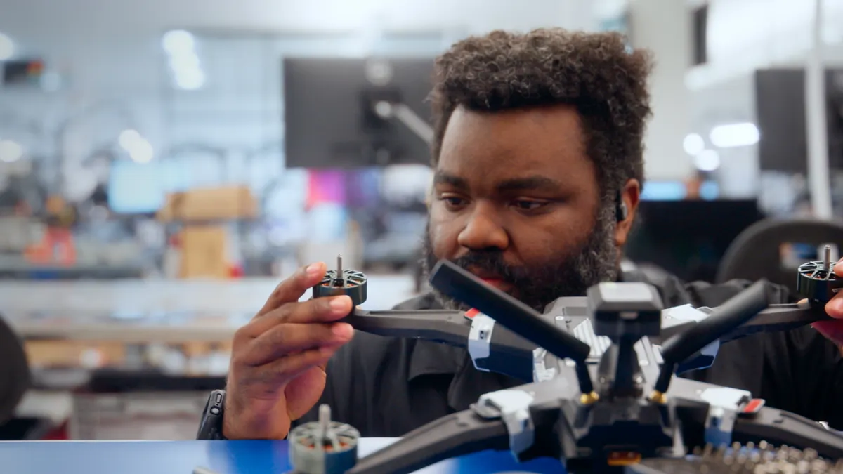 A person installing a part on a drone laying on a blue table.