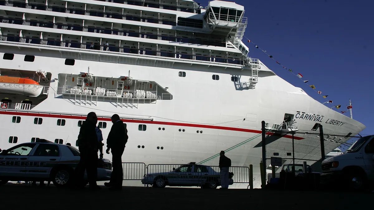 People stand on a dock below a large cruise ship