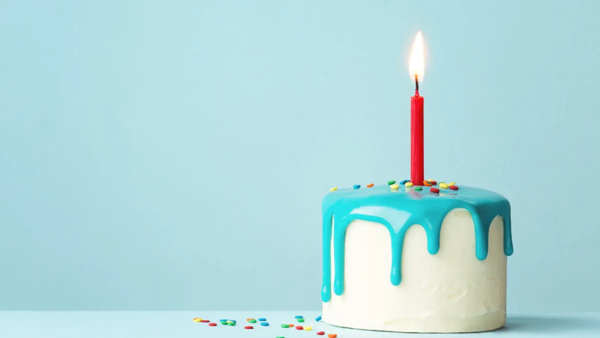 One candle sits on top of a small white cake with blue icing.