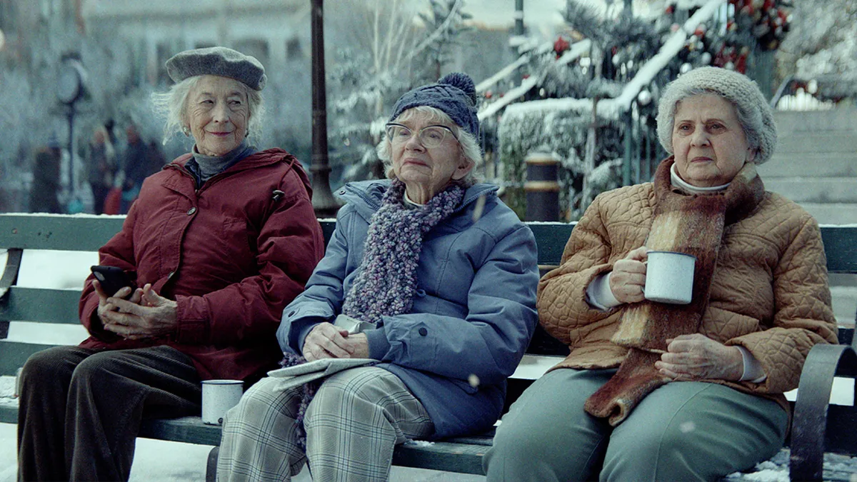 Three women are seen sitting outside on a snowy park bench as part of Amazon's "Joy Ride" 2023 holiday ad.