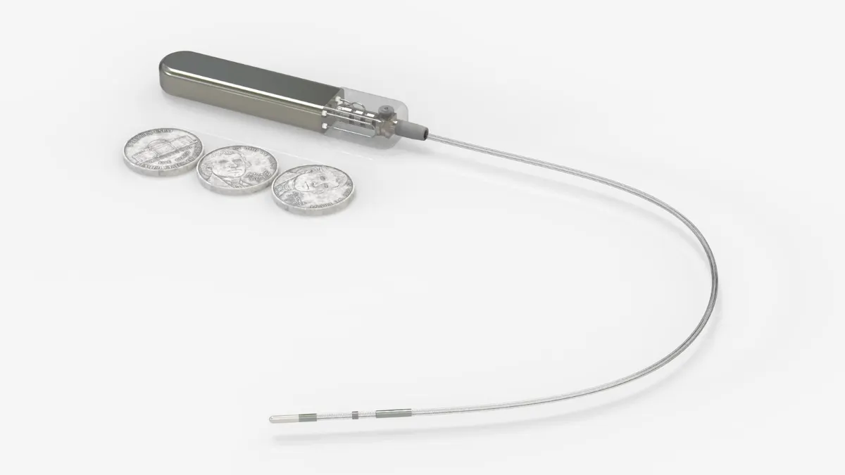 A rectangular, metallic device on a catheter sites next to three nickels.