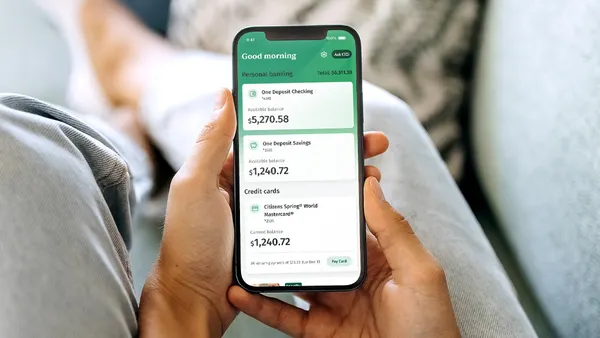 A person holds a mobile phone with a screen showing a bank account overview.