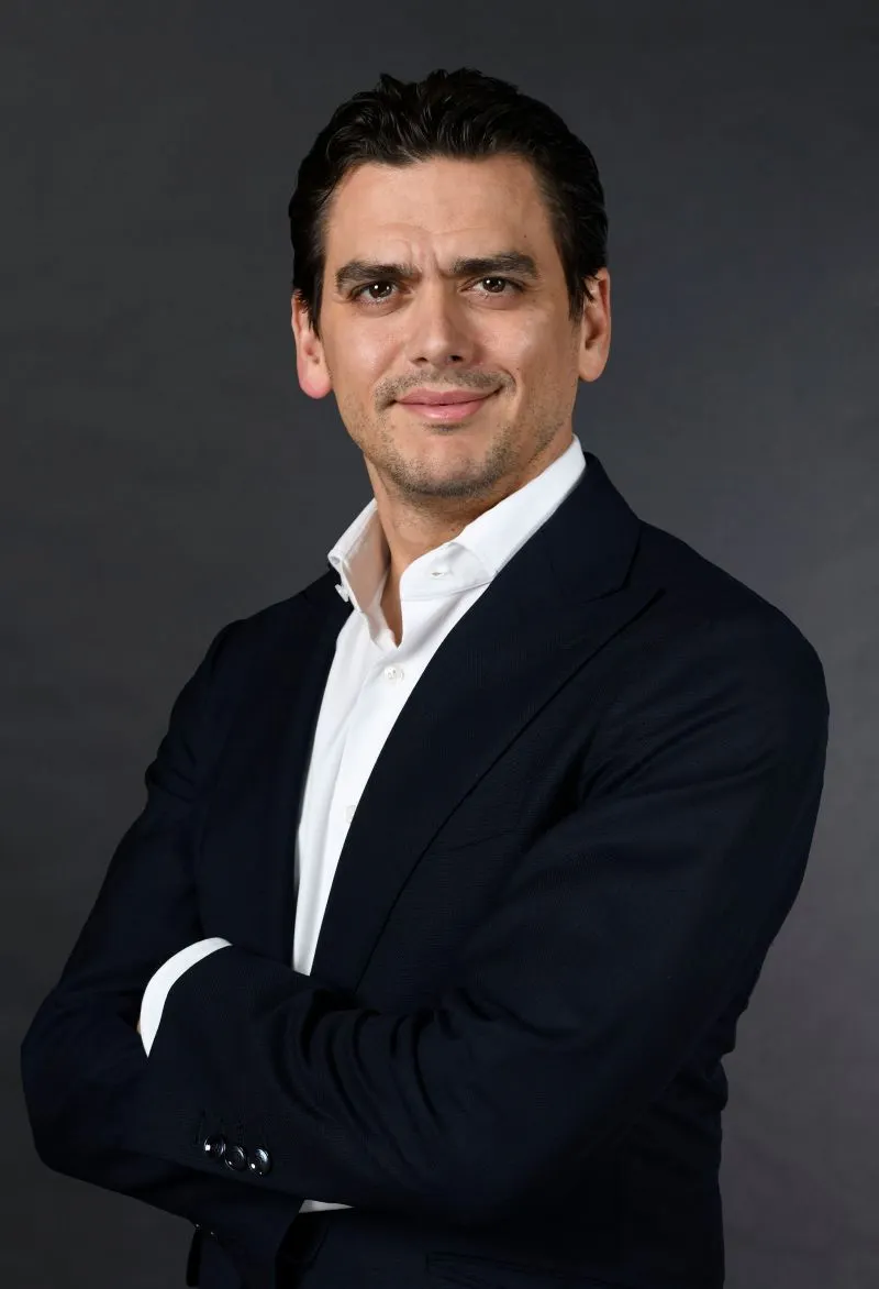A head and shoulders photo of a person with their arms crossed against a blue background.