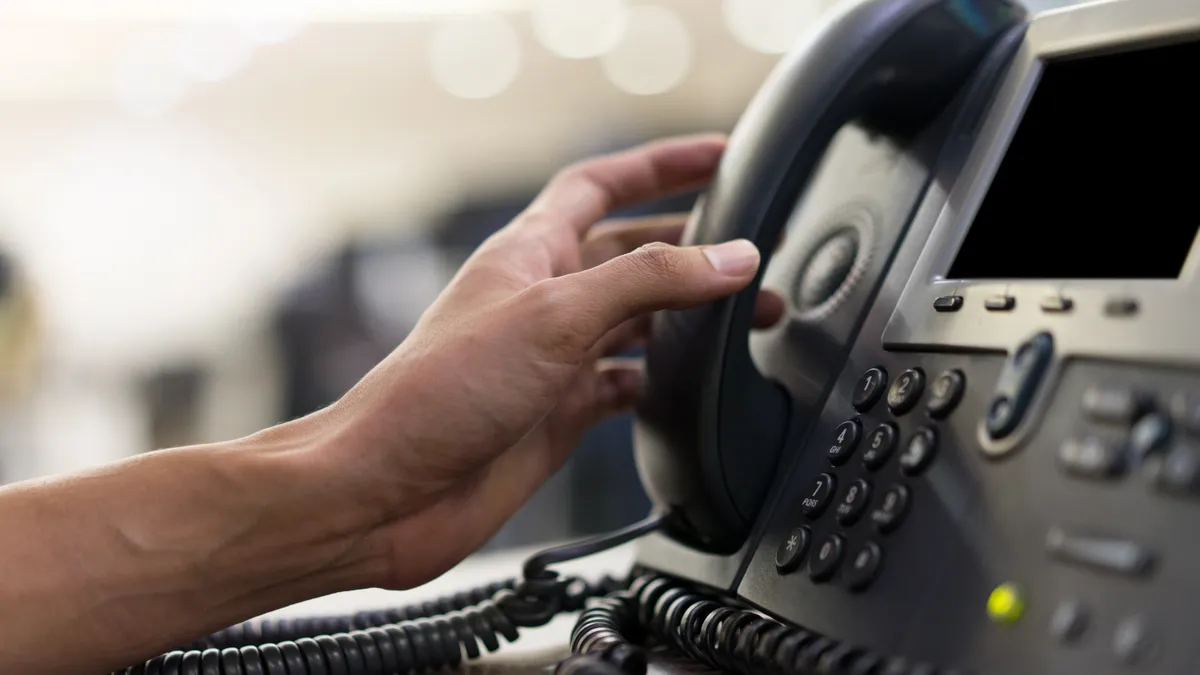 close up employee hand touching handset of telephone on desk for contact customer or receiving call.