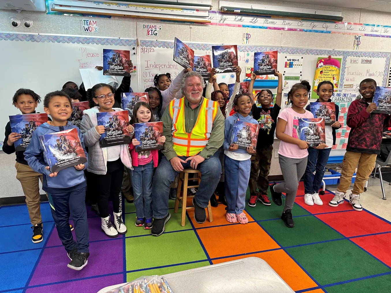 A group of elementary school students pose with a person in a construction vest.