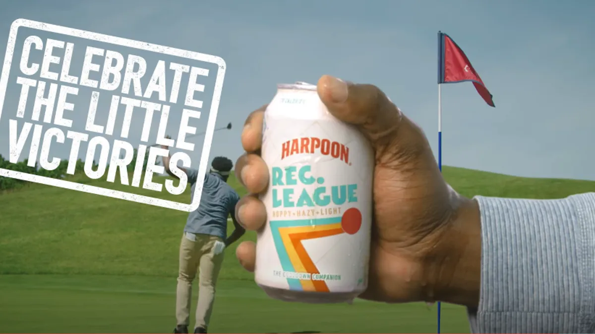 A hand holds a can of Harpoon Rec. League beer while a person plays golf in the background