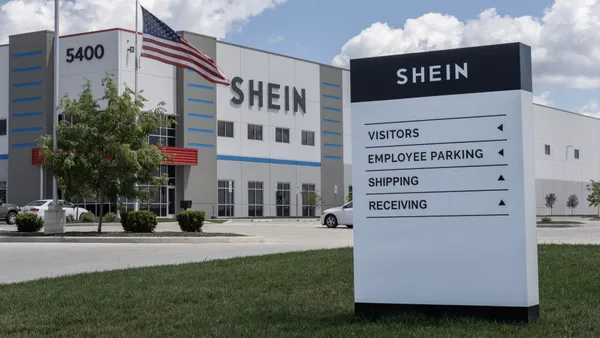 A closeup of a Shein sign directing people around its distribution center. The Shein building is seen in the background, with an American flag.