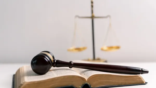 A gavel lays flat on top of an open Bible with the scales of justice displayed in the background.