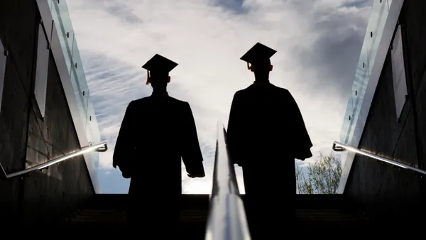 This is the silhouette of two college graduates in cap and gown climbing up a set of steps. This shot is backlit with bright morning sunshine in the background.