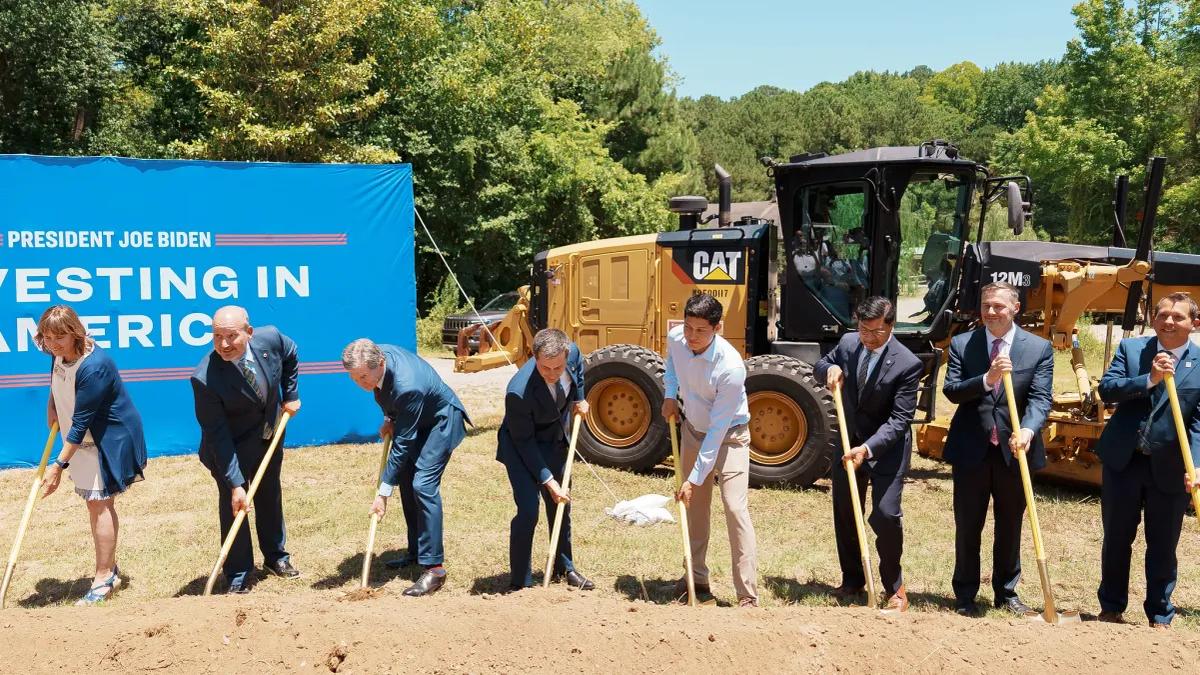 Men and women with shovels in front of a sign reading "President Joe Biden - Investing in America."