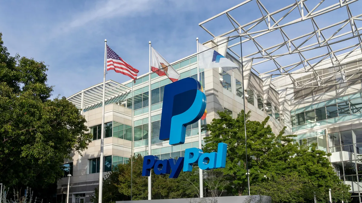 A large Paypal logo and sign are seen from a low angle, and a commercial building entrance is behind it. 