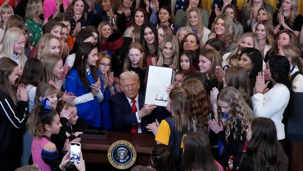 Trump holds up his signed executive order while surrounded by girl and women athletes.