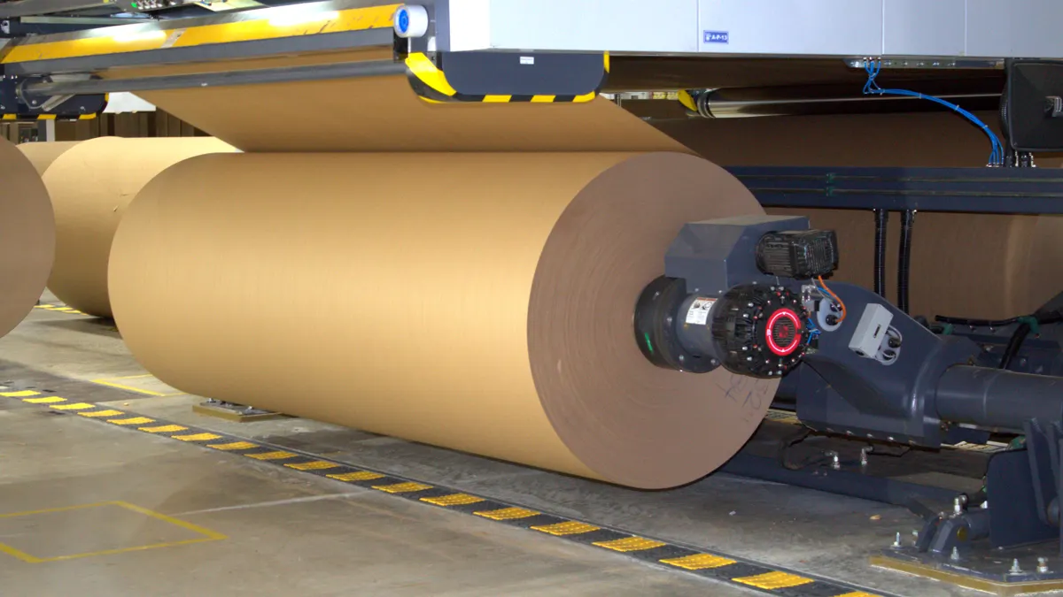 Large rolls of fiber material on industrial equipment inside a manufacturing facility.