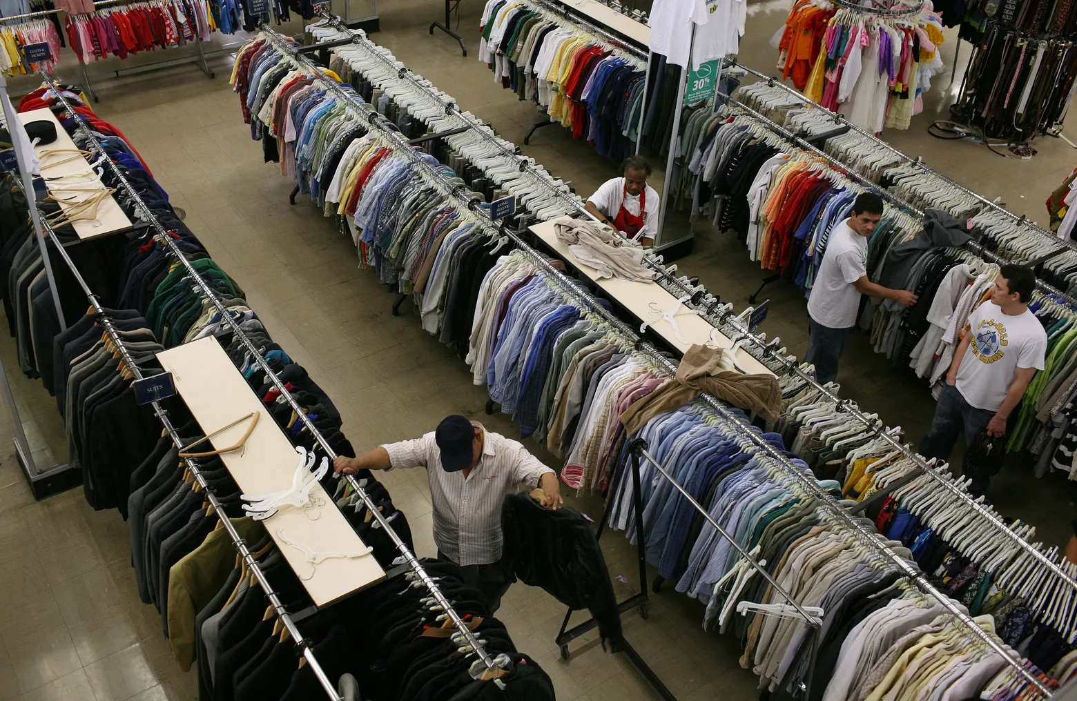 An aerial view of people shopping at a thrift store. They are looking through ailes of shirts.