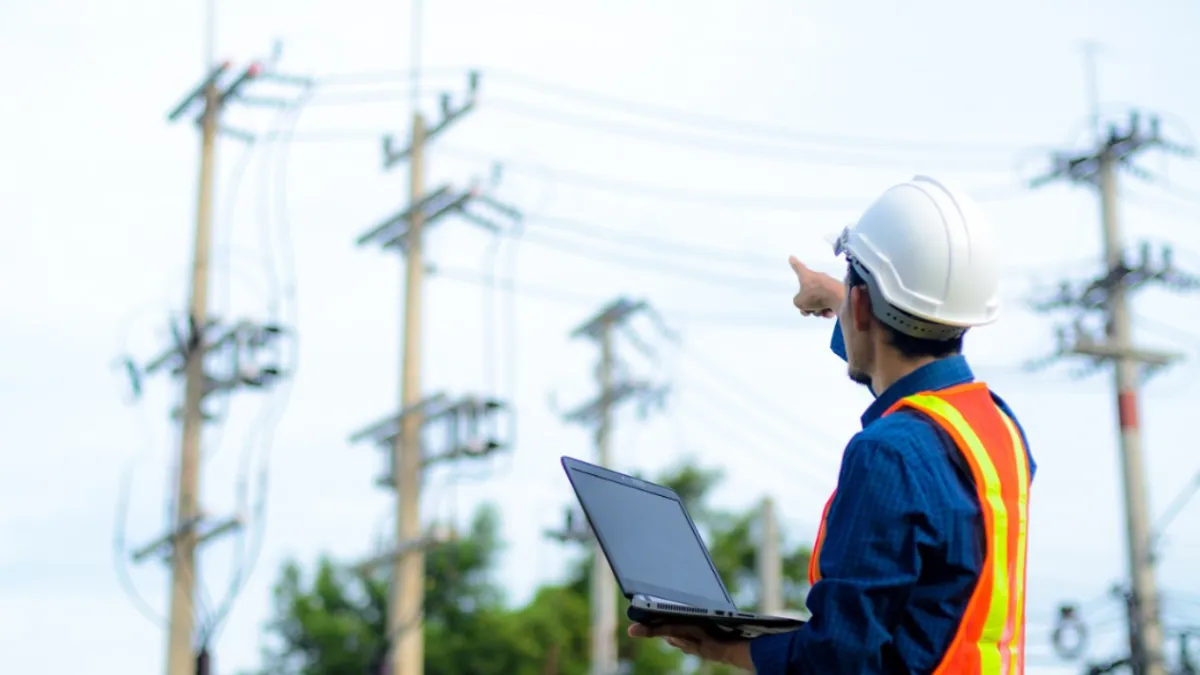 Person in hard hat and neon yellow safety vest pointing to electrical lines.