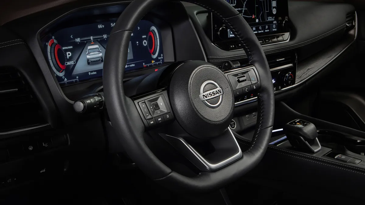 The black colored steering wheel with the Nissan logo on the horn pad of a 2021 Nissan Rogue SUV.