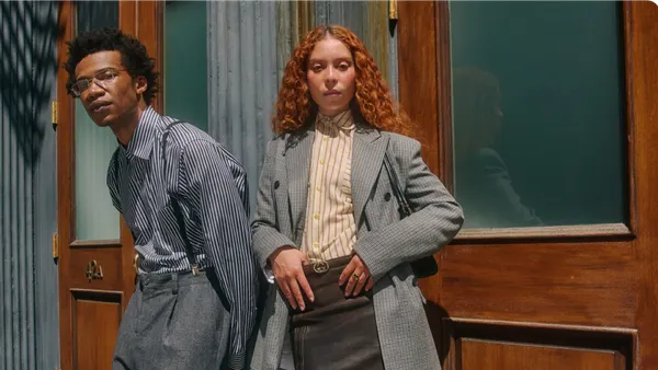 Two people stand next to each other in suiting looks.